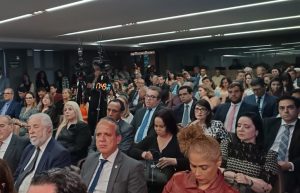 A imagem mostra a plateia sentada no auditório, entre homens e mulheres. Em primeiro plano está o vice-presidente do TJMMG, desembargador James Ferreira Santos, usando um terno cinza, camisa branca e gravata azul.