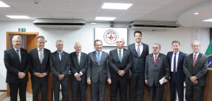 Na foto estão dez homens em pé na sala do Tribunal Pleno do TJMMG, entre desembargadores e desembargadores aposentados do TJMMG, além de desembargadores do TJMG. Eles estão lado a lado vestindo terno escuro e gravata. Ao fundo uma tela projeta o brasão do TJMMG