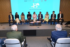 A foto mostra nove pessoas, entre homens e mulheres. Eles estão em um palco, diante de uma mesa de centro, e em primeiro plano aparecem duas autoridades com fardas militares. Ao fundo há um telão com a logomarca do Banco de Sentenças, formado pela letra B estilizada com um malhete, como é chamado o martelo que simboliza a Justiça