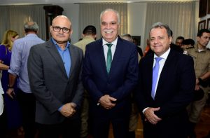 A foto mostra três homens em uma sala com diversas pessoas. Eles estão em pé, todos de terno. Ao centro está o desembargador coronel Rúbio Paulino Coelho, que sorri para a foto. Ele tem cabelos e bigode grisalhos. Ao lado direito da imagem está o coronel Giovanne Gomes da Silva, e à esquerda o coronel veterano Ricardo Geraldo de Oliveira Viana