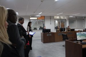 Imagem mostra um grupo de estudantes de Direito, entre homens e mulheres, em uma sala de audiências. Eles observam três militares fardados que fazem parte do Conselho Permanente de Justiça da 4ª Auditoria de Justiça Militar, que estão sentados atrás de uma bancada de madeira