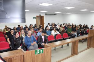 Imagem mostra a plateia presente na sala do Tribunal Pleno do TJMMG, entre homens e mulheres, contando com 52 estudantes de Direito. Eles estão sentados em poltronas vermelhas, em uma sala de paredes brancas