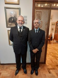 A imagem mostra o novo integrante do IGHMG, coronel José Anísio Moura vestindo terno e gravata preta, ele tem barba branca e está com os braços para trás. Ao seu lado está o desembargador Sócrates Edgard dos Anjos também de terno e gravata preta, ele tem bigode branco e está com as mãos cruzadas à frente do corpo