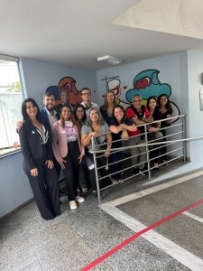 A imagem mostra 12 pessoas entre homens e mulheres que realizaram a doação de sangue. Eles posam para a foto em uma rampa atrás de um corrimão de metal. As paredes são azul claro e possuem grafittes. O chão é cinza e apresenta detalhes brancos