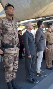 A imagem mostra o novo comandante do CME, coronel Israel Calixto Júnior, vestindo farda oficial da PMMG. Ao seu lado está o corregedor da Justiça Militar mineira, desembargador coronel Sócrates Edgard dos Anjos, vestindo terno cinza e gravata preta. Eles estão de pé em um tablado coberto