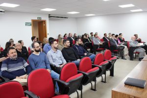A imagem mostra o público participante da reunião, composta por magistrados e servidores, entre homens e mulheres, sentados em cadeiras vermelhas