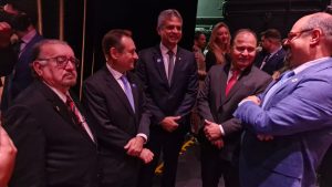 A imagem mostra cinco homens em pé, todos vestindo terno. O mais à esquerda é o presidente do TJMMG, que usa óculos e gravata listrada em vermelho e preto.