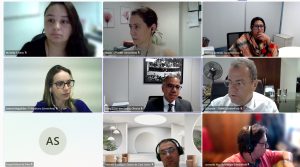 A imagem mostra nove participantes durante a reunião virtual do Ciclo de Gestão de Metas, organizados em mosaico de videochamada. Entre eles, homens e mulheres em diferentes ambientes, alguns com fones de ouvido e outros em escritórios. Os participantes acompanham atentamente a reunião a partir de seus locais de trabalho. São ambientes institucionais e a maioria conta com quadros decorativos ao fundo. Ao centro, um dos participantes veste terno
