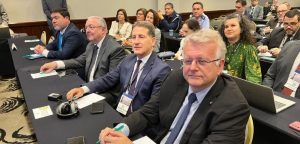 A imagem mostra diversas pessoas, entre homens e mulheres, sentados em auditório durante o Congresso Internacional de Direito Militar. Em primeiro plano, ao centro, está o desembargador Fernando Antônio Nogueira Galvão da Rocha, que veste terno azul-marinho e gravata roxa.