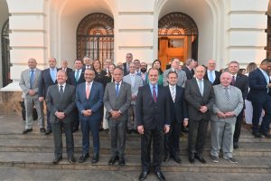 A imagem mostra um grupo de pessoas, entre homens e mulheres, posando para foto nos degraus de um prédio histórico de fachada clara, com grandes arcos e janelas ornamentadas. Na primeira fileira, o terceiro da esquerda para a direita é o vice-presidente do TJMMG, de terno cinza, camisa clara e gravata azul.