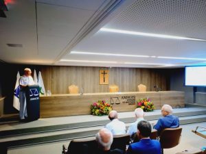A imagem mostra o ministro Leonardo Puntel proferindo a palestra de encerramento do seminário promovido pela EJM. Ele veste farda branca e fala de uma tribuna. À frente está a plateia, sentada em poltronas escuras