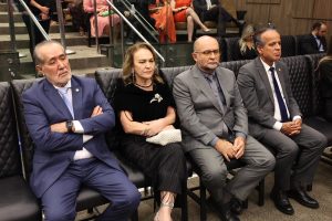 A imagem mostra quatro pessoas sentadas no Auditório do Tribunal Pleno do TJMG. O primeiro à direita da imagem é o desembargador vice-presidente James Ferreira Santos, de terno cinza, camisa branca e gravata escura.