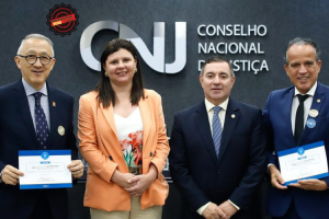 A imagem mostra quatro autoridades posando para foto em frente ao painel do CNJ. Da esquerda para a direita, estão o corregedor-geral da Justiça Militar do Estado de São Paulo, usando terno escuro e segurando um certificado; a conselheira do CNJ, vestindo blazer claro sobre blusa estampada; o secretário de Estratégia e Projetos do CNJ, de terno escuro e gravata; e o vice-presidente do TJMMG, também de terno, segurando um certificado. Todos estão em pé, lado a lado, em ambiente institucional.