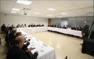 A imagem mostra uma ampla sala, com uma mesa de reunião ocupada por representantes dos Tribunais de Justiça e Tribunais de Justiça Militar dos estados, entre homens e mulheres. Ao centro está o presidente do CNJ, e na ponta direita da mesa está o vice-presidente do TJMMG