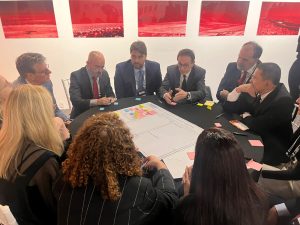 A imagem mostra uma ampla sala, com uma mesa de reunião ocupada por representantes dos Tribunais de Justiça e Tribunais de Justiça Militar dos estados, entre homens e mulheres. Ao centro está o presidente do CNJ, e na ponta direita da mesa está o vice-presidente do TJMMG