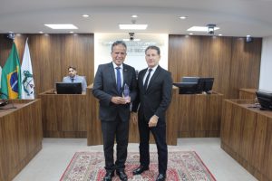 A imagem mostra os desembargadores vestindo terno escuro. Eles estão no Tribunal Pleno, em que há três bandeiras ao fundo e uma parede de madeira. 