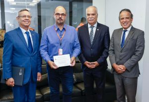 A imagem mostra quatro homens em pé, um ao lado do outro. Da esquerda para a direita está o desembargador Osmar Duarte Marcelino; o vice-governador Mateus Simões, segurando um convite em mãos; o desembargador Rúbio Paulino Coelho e o desembargador James Ferreira Santos. Todos vestem trajes formais.