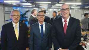 A imagem mostra três homens em pé, um ao lado do outro. Ao centro está o desembargador Osmar Duarte Marcelino, vestindo terno azul escuro e gravata azul; à esquerda da imagem está o desembargador Silvio Hiroshi Oyama, vestindo terno preto e gravata amarela; à direita está o desembargador Rodrigo Mohr Picon, vestindo terno preto e gravata vermelha.