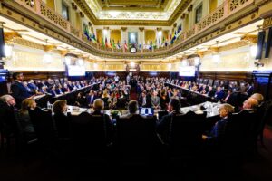 A imagem mostra o Salão Nobre da sede TJSP repleto de autoridades convidadas para a abertura do XX Encontro do Consepre. Um grupo de autoridades está disposto em semicírculo, enquanto outro está sentado ao centro. O salão tem paredes com pé direito alto, com um mezanino, tudo em tom claro com detalhes dourados e madeira. No mezanino estão dispostas bandeiras de todos os estados com representatividade no Consepre 