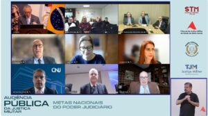 A imagem mostra momento da transmissão da audiência pública pelo YouTube. Em um fundo azul-claro, aparecem nove quadros de videoconferência com os participantes da audiência. No quadro superior direito, estão os três representantes do TJMMG sentados em uma mesa de reuniões. Na lateral direita da imagem, estão os logotipos dos tribunais participantes e, abaixo, uma intérprete de Libras. Na parte inferior esquerda está escrito: Audiência Pública da Justiça Militar. Metas Nacionais do Poder Judiciário.