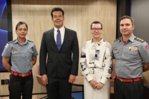 A imagem mostra quatro pessoas, na Sala Diamante do TJMMG, em pé, lado a lado. Nela estão, nos extremos da imagem, a major Débora Cristina Carvalho Brandão e o coronel João Guilherme Britto Vieira, ambos vestindo uniforme em tons de cinza do CBMMG. Ao centro, estão o desembargador Fernando José Armando Ribeiro, vestindo terno preto, camisa clara e gravata azul; e a juíza de Direito titular do Juízo Militar Daniela de Freitas Marques, vestindo camisa estampada em preto e branco e saia branca. O ambiente possui parede revestida em madeira.