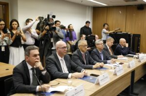 A imagem mostra cinco pessoas sentadas à mesa, em uma reunião no STF. Da direita para a esquerda, o segundo é o desembargador Osmar Duarte Marcelino, que veste terno cinza-escuro e gravata lilás. Ao seu lado estão os desembargadores Silvio Hiroshi Oyama, de terno cinza-escuro e gravata rosa, e Rodrigo Mohr Picon, também de terno cinza-escuro e gravata branca. Ao fundo, diversas pessoas acompanham e registram a reunião com câmeras e celulares.