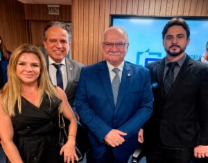 A imagem mostra quatro pessoas em pé. A segunda pessoa, da esquerda para a direita, é o desembargador Jâmes Ferreira Santos, vestindo terno cinza, camisa branca e gravata azul. Ao seu lado, está o ministro Edson Faquin, de terno azul, camisa branca e gravata azul clara. Ao lado dele, está o servidor Tiago Augusto Duarte Pereira, usando terno preto, camisa cinza e gravata preta. A mulher do grupo é a servidora Tatiana Reis Teixeira, usando vestido preto. Ao fundo, aparece uma parede revestida em madeira.