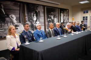 A imagem mostra uma mesa composta por nove autoridades, entre homens e mulheres. A terceira pessoa é o desembargador Osmar Duarte Marcelino, vestindo terno azul, camisa branca e gravata azul. Ao fundo, aparecem quadros com fotografias em preto e branco.