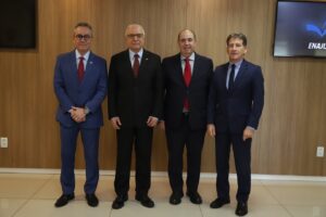 A imagem mostra quatro homens em pé, lado a lado. Da direita para a esquerda, estão o desembargador Fernando Antônio Nogueira Galvão da Rocha, vestindo terno azul-escuro e gravata escura; o desembargador Paulo Adib Casseb, de terno preto e gravata vermelha; o ministro Péricles Aurélio Lima de Queiroz, de terno preto e gravata vermelha com destalhes brancos; e o desembargador Amilcar Fagundes Freitas Macedo, vestindo terno azul e gravata vermelha.