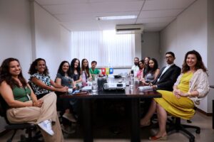 A imagem mostra um grupo de 12 pessoas, entre homens e mulheres, sentadas em uma mesa de reunião do TJMMG. Todos vestem roupas sociais.